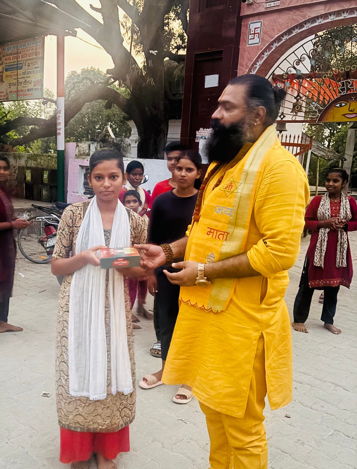 कबीर जी महाराज गाँव की बच्ची को प्रसाद देते हुए — पृष्ठभूमि में धाम का प्रवेश द्वार